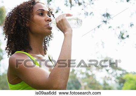 Stock Image - Mid adult woman drinking from water bottle. Fotosearch