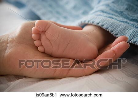 Stock Image - Mid adult woman holding baby boy's foot. Fotosearch