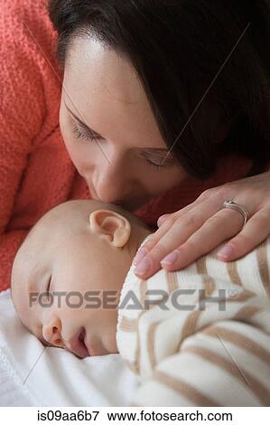 Stock Photo - Mid adult woman kissing baby son, close up. Fotosearch