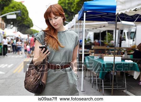 Stock Image - Mid adult woman looking at mobile phone in city. Fotosearch
