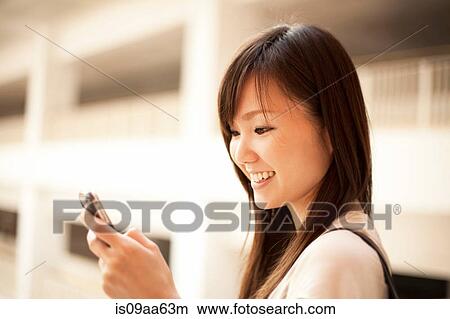 Picture - Mid adult woman looking at mobile phone, smiling. Fotosearch