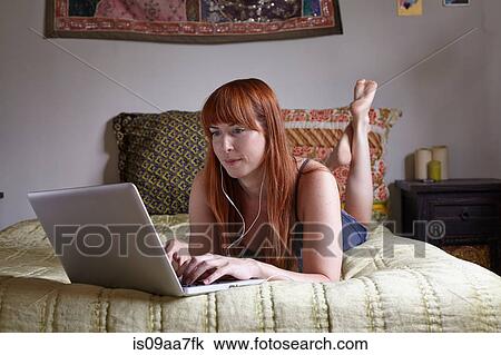 Stock Image - Mid adult woman lying on bed using laptop. Fotosearch