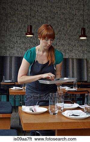 Stock Photograph - Mid adult woman preparing table in restaurant. Fotosearch
