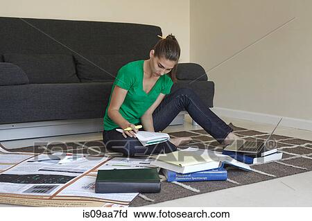 Stock Image - Mid adult woman sitting on floor studying. Fotosearch