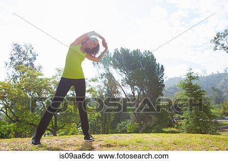 Stock Image - Mid adult woman stretching in park. Fotosearch