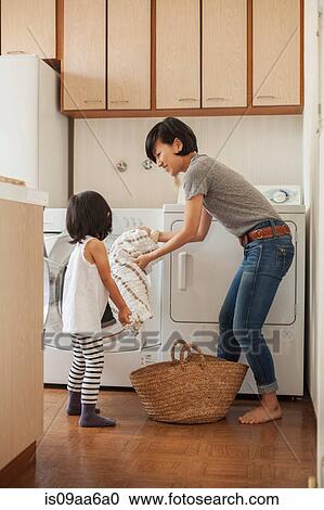 Stock Image - Mother and daughter putting towel into washing machine. Fotosearch