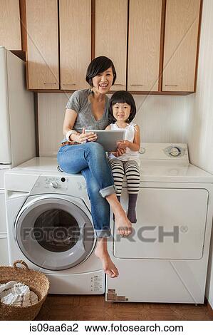 Mother and daughter sitting on washing machine using tablet View Large Photo Image Stock Image - Mother and daughter sitting on washing machine using tablet. Fotosearch