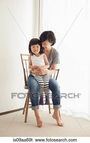 Stock Photograph - Mother and daughter sitting on wooden chair, portrait. Fotosearch