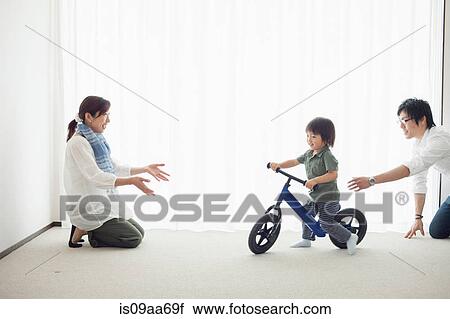 Stock Image - Parents with son learning to ride bicycle. Fotosearch