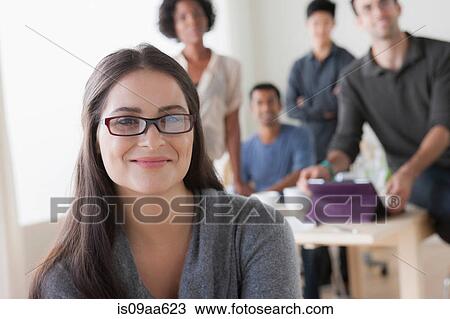 Stock Image - Portrait of young female office worker in front of colleagues. Fotosearch