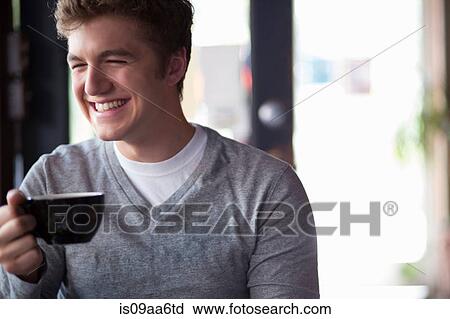 Stock Image - Portrait of young man in cafe holding cup. Fotosearch