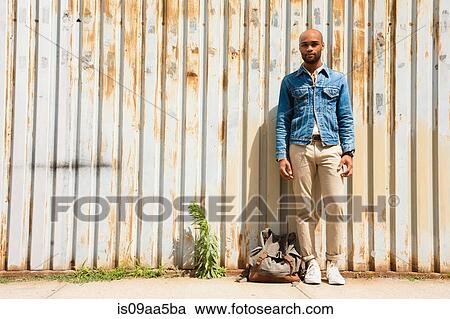 Stock Image - Portrait of young man in front of corrugated fence. Fotosearch