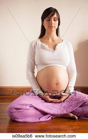 Stock Photograph - Pregnant woman meditating whilst sitting on floor. Fotosearch