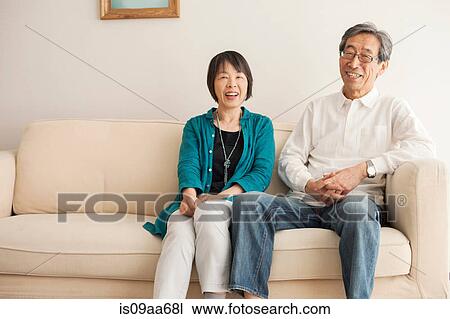 Stock Image - Senior couple sitting on sofa, portrait. Fotosearch