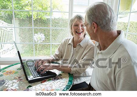 Stock Image - Senior couple using laptop in conservatory. Fotosearch