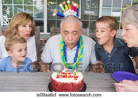 Senior man blowing out candles on birthday cake with family View Large Photo Image Stock Image - Senior man blowing out candles on birthday cake with family. Fotosearch