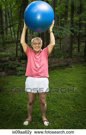 Stock Photo - Senior man holding up exercise ball, portrait. Fotosearch