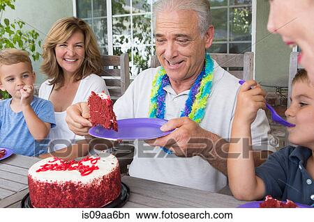 Picture - Senior man serving slice of birthday cake at party with family. Fotosearch