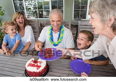 Picture - Senior woman serving slice of birthday cake at party with family. Fotosearch