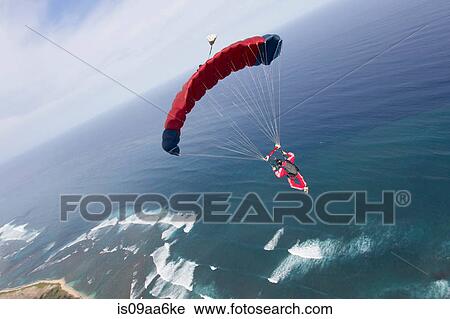Stock Image - Skydiver with red parachute above Honolulu, Hawaii. Fotosearch