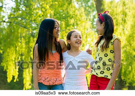 Stock Image - Three girls in park with arms around each other. Fotosearch