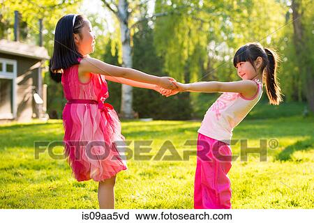 Stock Image - Two girls holding hands in garden. Fotosearch