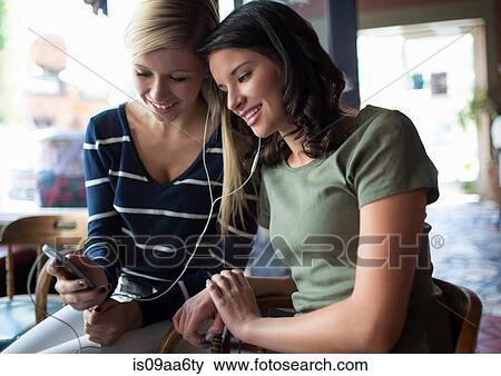 Two teenage girls sharing earphones in coffee house View Large Photo Image Stock Photo - Two teenage girls sharing earphones in coffee house. Fotosearch