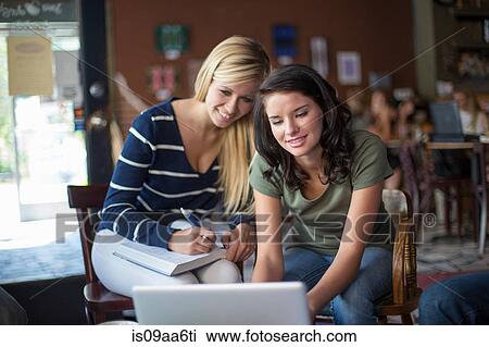 Stock Image - Two teenage girls using textbooks and computer in cafe. Fotosearch