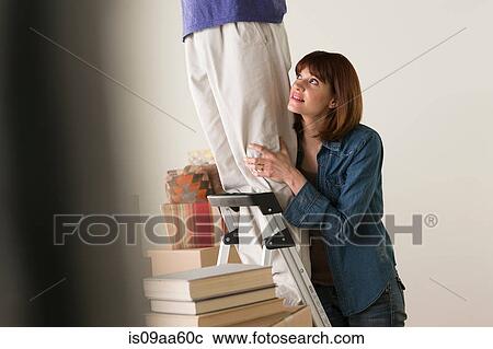 Stock Image - Woman holding onto man on stepladder. Fotosearch