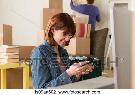 Woman looking at cellphone whilst moving house View Large Photo Image Stock Image - Woman looking at cellphone whilst moving house. Fotosearch