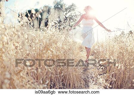 Stock Image - Woman walking through field touching grasses. Fotosearch