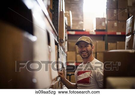 Stock Image - Worker and cardboard boxes stored in warehouse. Fotosearch