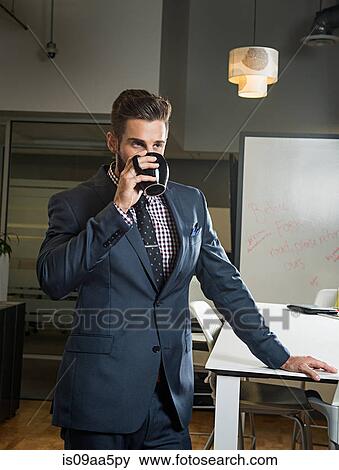 Stock Photo - Young businessman drinking from cup in office. Fotosearch