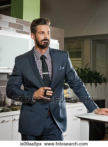 Stock Photo - Young businessman holding cup in office kitchen. Fotosearch