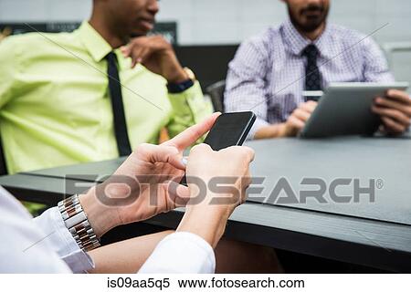Stock Photography - Young businesswoman looking at smartphone in meeting. Fotosearch