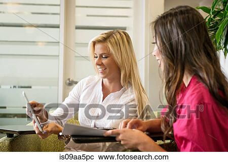 Stock Image - Young businesswomen looking at digital tablet in meeting. Fotosearch