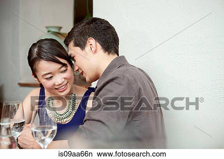 Picture - Young couple in restaurant, man whispering. Fotosearch