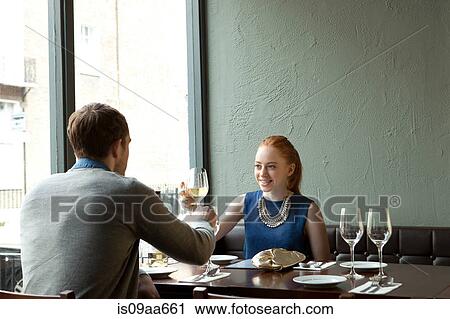 Stock Image - Young couple in restaurant toasting wine glasses. Fotosearch