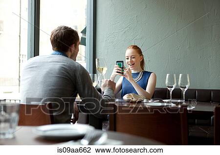 Stock Image - Young couple in restaurant, woman using cell phone. Fotosearch