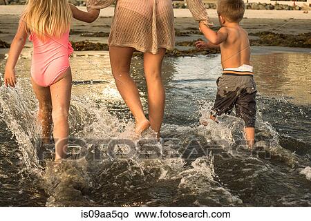 Picture - Young family paddling through water, rear view. Fotosearch