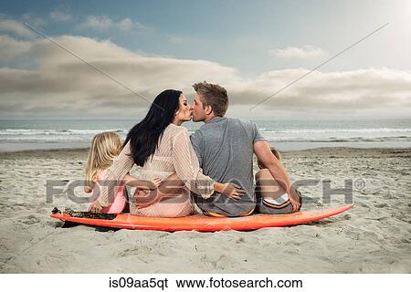 Young family sitting on surfboard on beach with parents kissing View Large Photo Image Stock Photograph - Young family sitting on surfboard on beach with parents kissing. Fotosearch