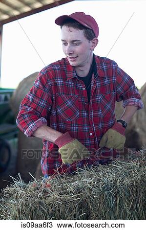Stock Image - Young farmer lifting straw bale. Fotosearch