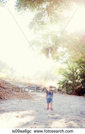 Stock Image - Young female toddler with hands in pockets on dirt track. Fotosearch
