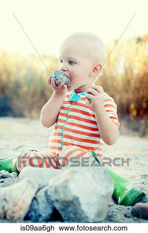 Stock Image - Young male toddler tasting campfire stones. Fotosearch