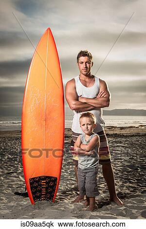 Young man and son standing with surfboard on beach, portrait View Large Photo Image Stock Image - Young man and son standing with surfboard on beach, portrait. Fotosearch