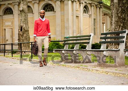 Stock Image - Young man carrying briefcase through park. Fotosearch