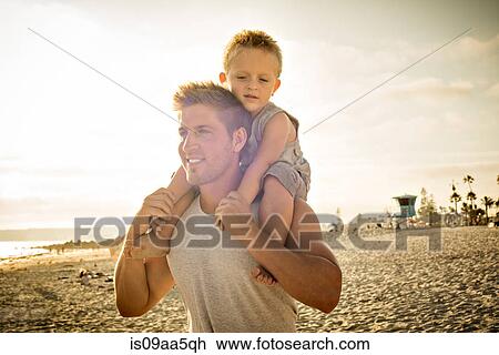 Young man carrying son on shoulders on beach View Large Photo Image Stock Image - Young man carrying son on shoulders on beach. Fotosearch