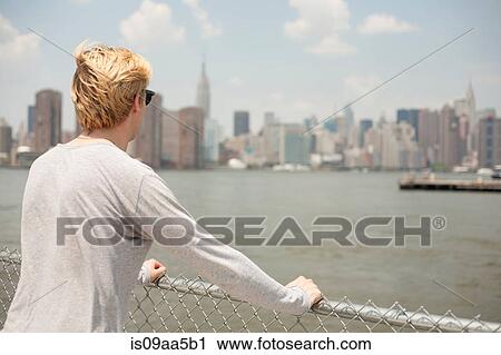 Stock Image - Young man looking at city skyline, Brooklyn, New York City, USA. Fotosearch
