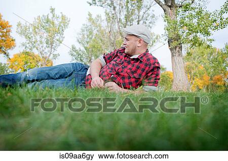 Young man lying on grass in park View Large Photo Image Stock Photo - Young man lying on grass in park. Fotosearch