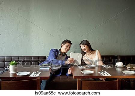 Stock Image - Young man showing young woman digital tablet in restaurant. Fotosearch